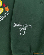 Close-up of custom sleeve embroidery featuring Gilmore Girls text and a coquette bow on a forest green sweater sleeve