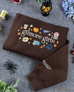Folded brown Gilmore Girls crewneck sweater with cozy fall aesthetic decor and sleeve embroidery detail