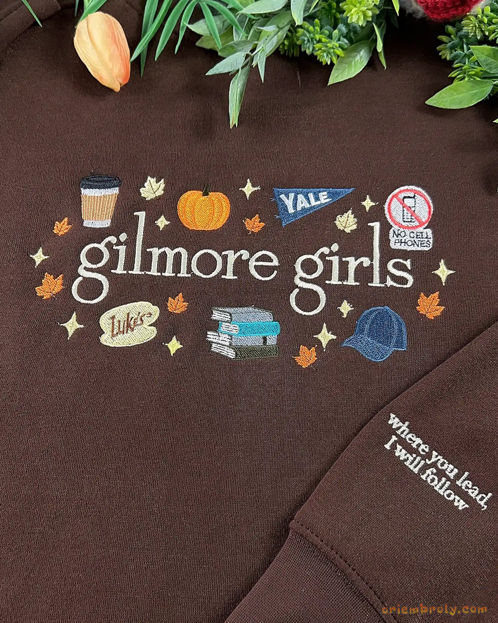 Close-up of Gilmore Girls autumn embroidery featuring a coffee cup, pumpkin, Yale pennant, and books on a brown sweater
