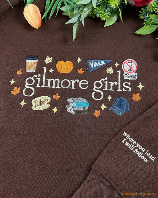 Close-up of Gilmore Girls autumn embroidery featuring a coffee cup, pumpkin, Yale pennant, and books on a brown sweater