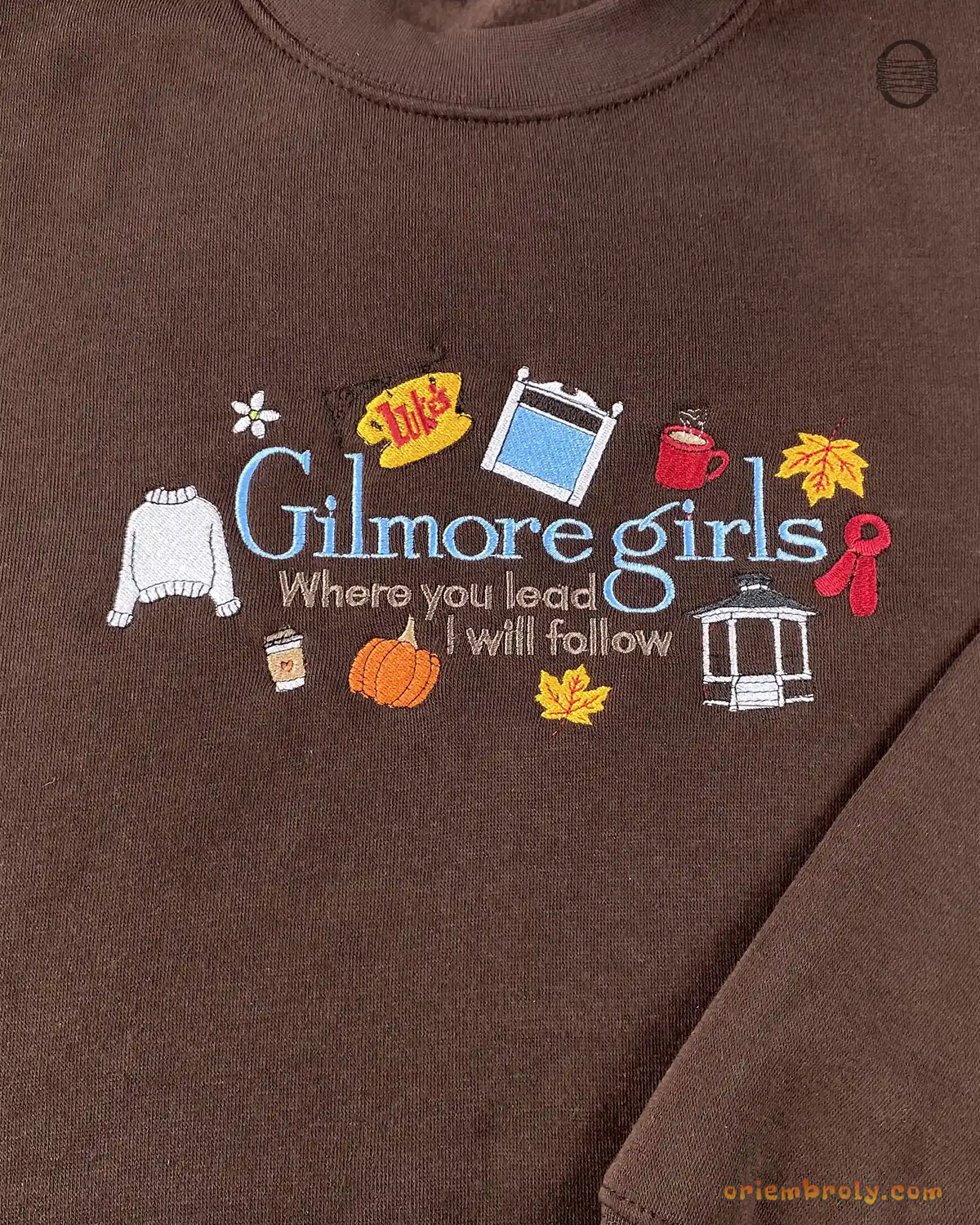 Close-up of Gilmore Girls Where You Lead I Will Follow embroidery with coffee cups and autumn decor on a brown sweater
