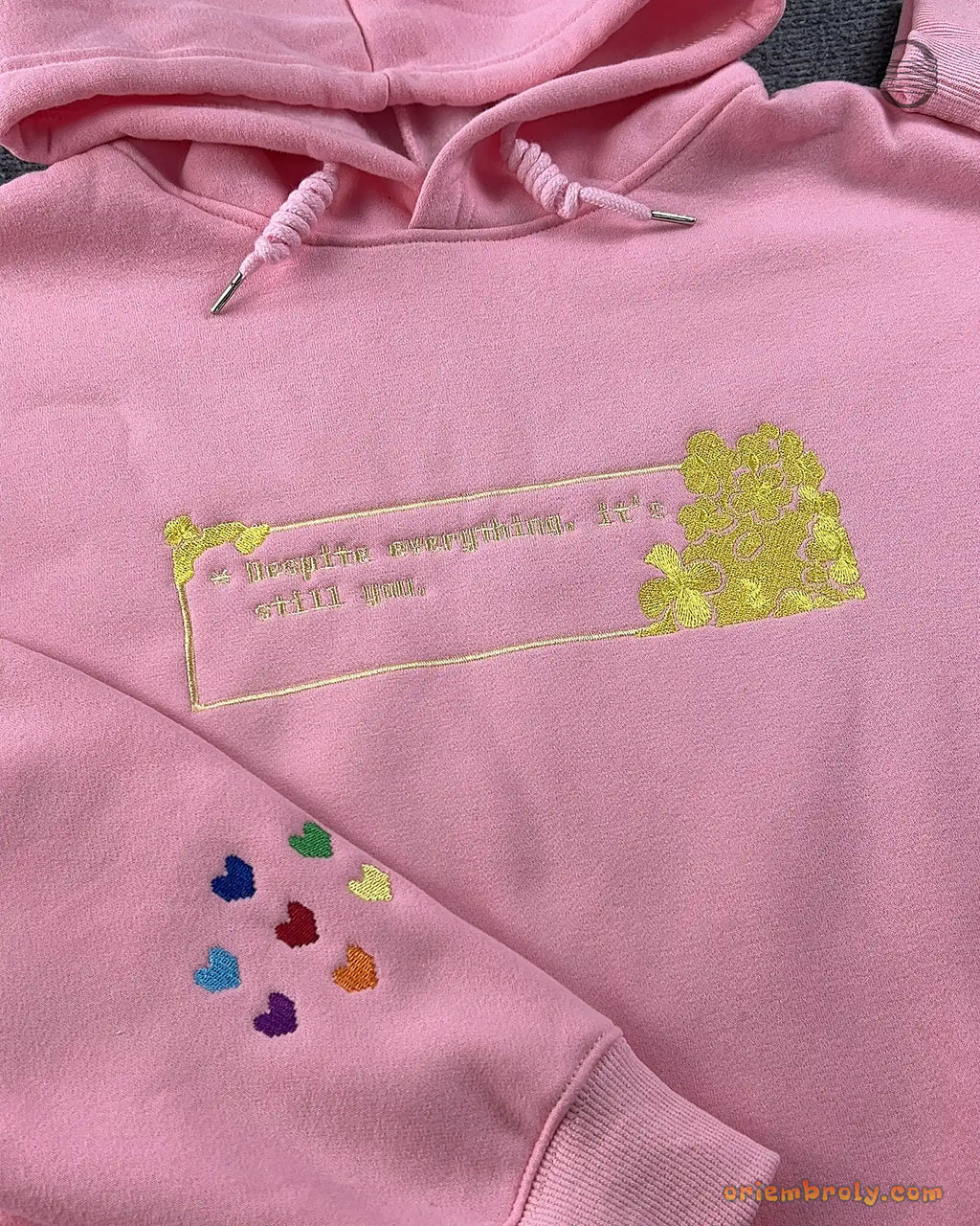 Close-up of gold embroidered quote with hearts box and colorful rainbow hearts sleeve detail on a pink hoodie