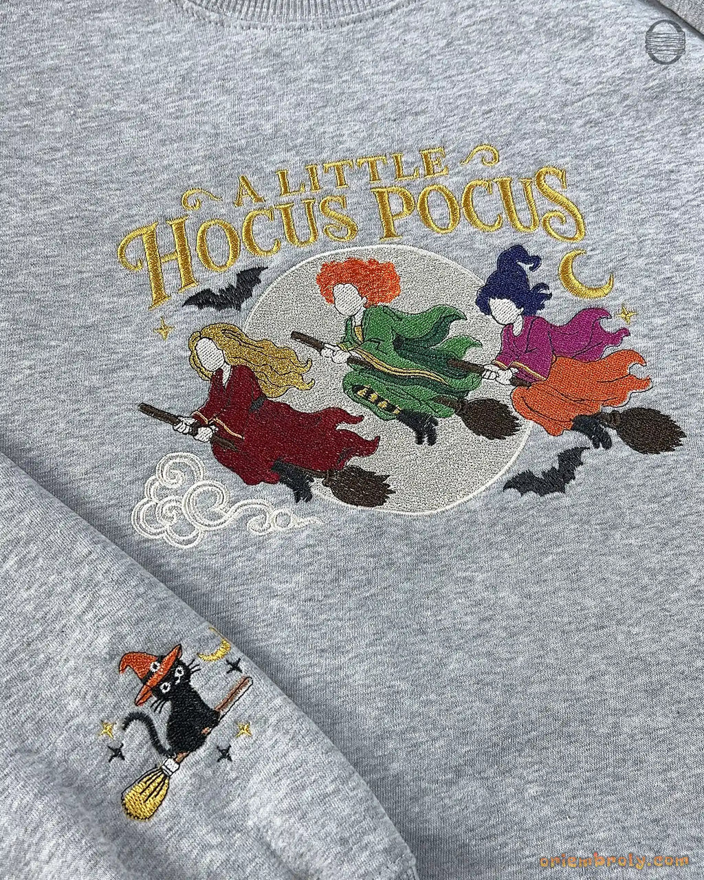 Close-up of ash gray sweatshirt embroidered with A Little Hocus Pocus text, colorful witch hair, and flying broomsticks.