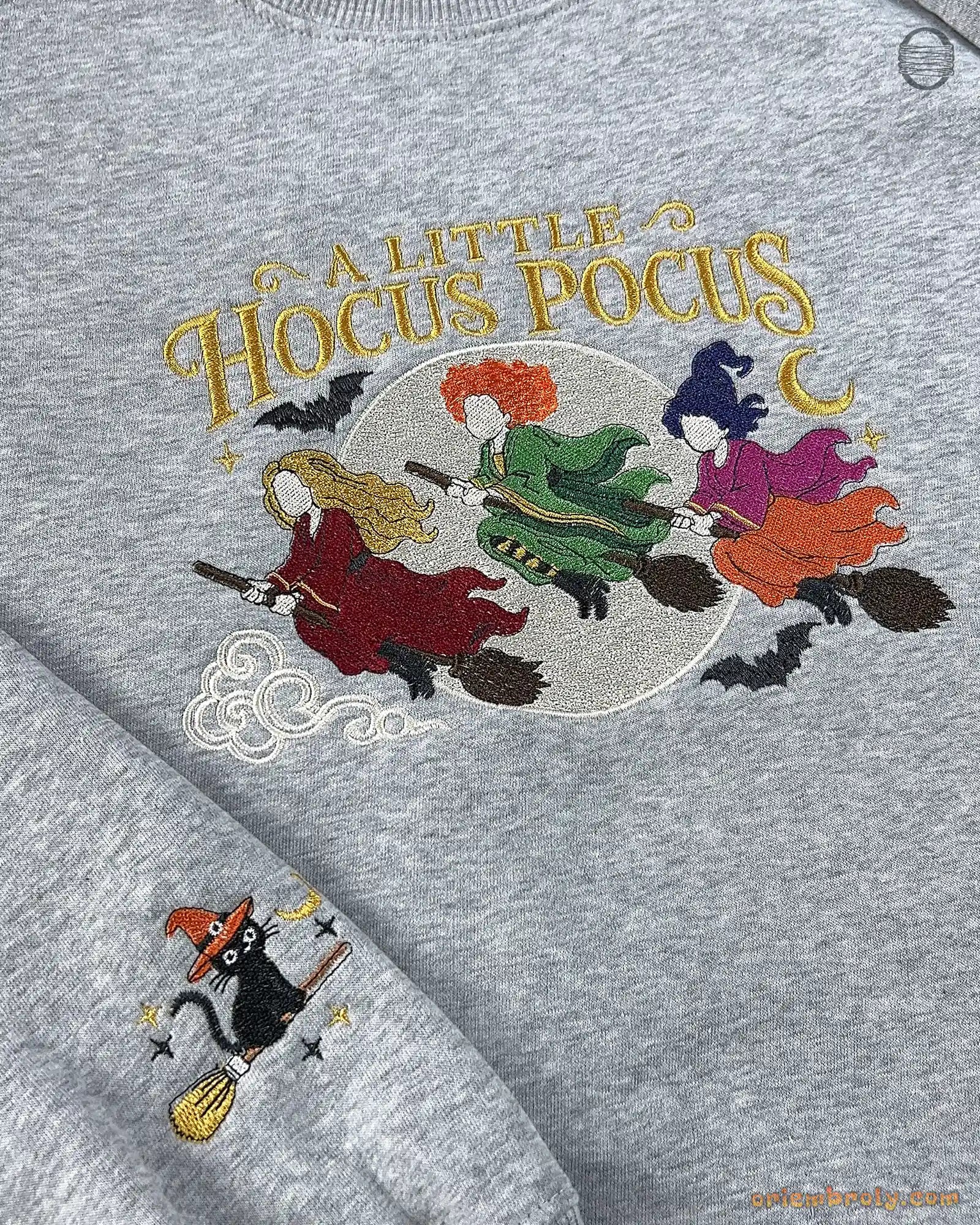 Close-up of ash gray sweatshirt embroidered with A Little Hocus Pocus text, colorful witch hair, and flying broomsticks.