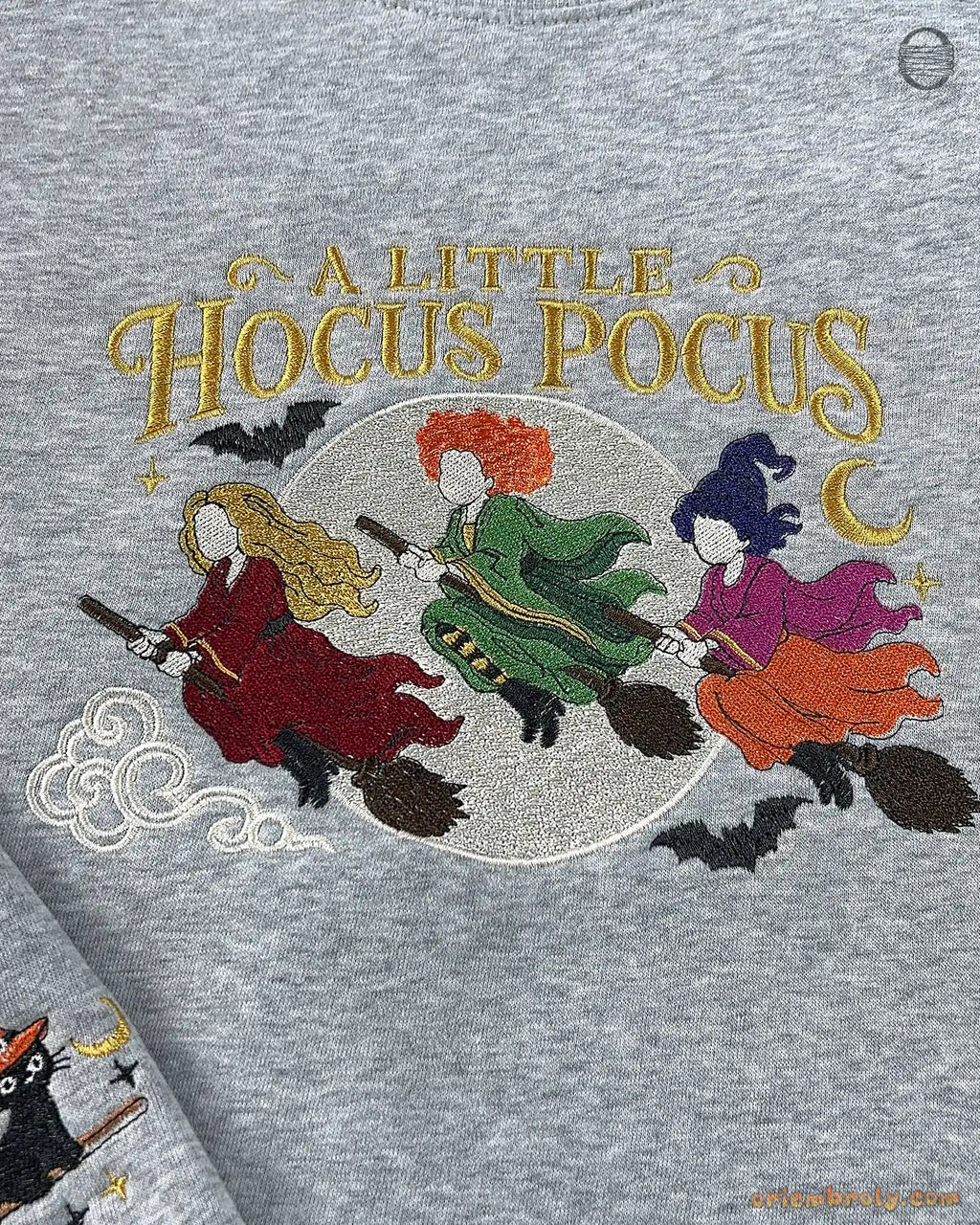 Detailed view of colorful embroidery on a gray sweatshirt featuring flying witches, full moon, bats, and stars.