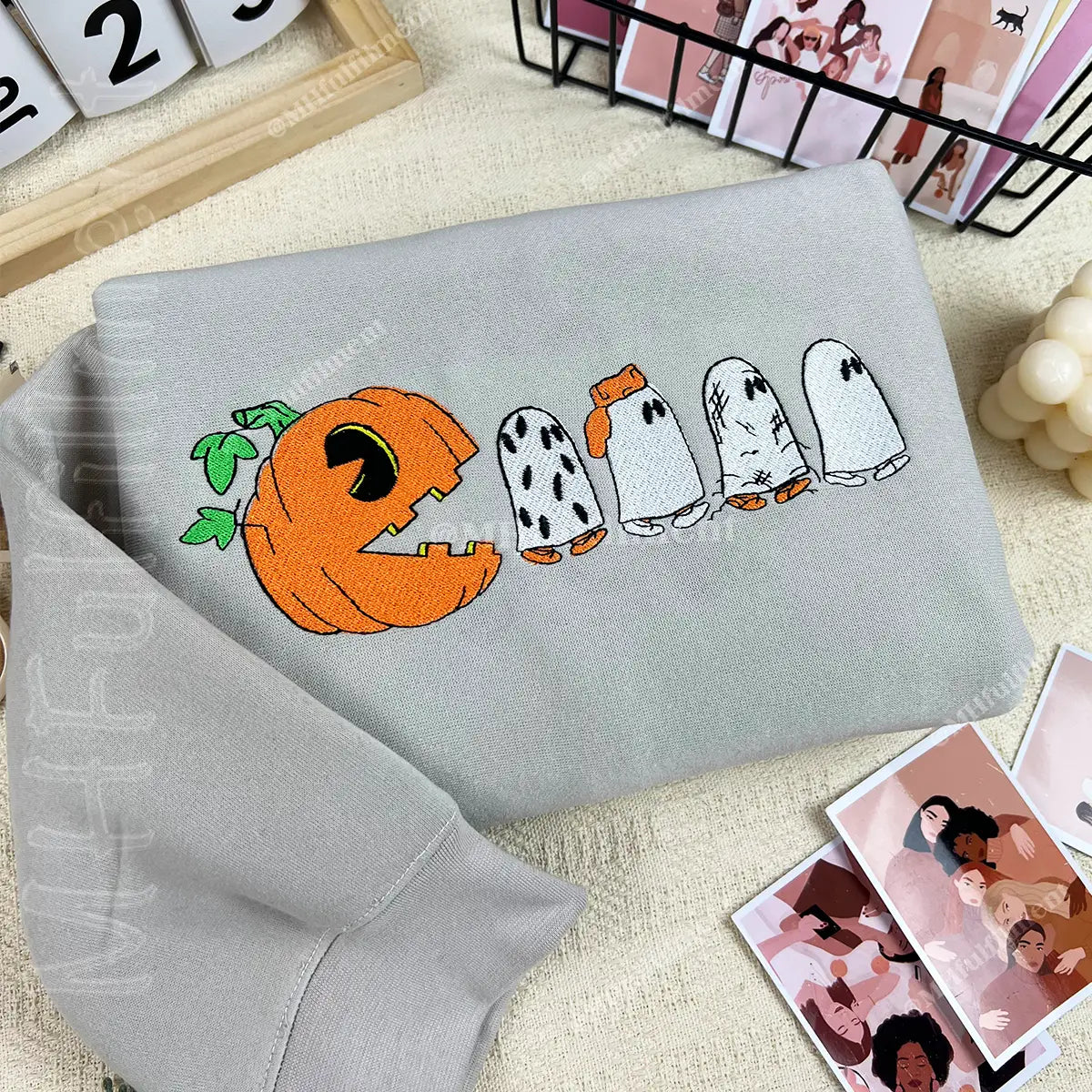 Gray sweatshirt with Halloween-themed design featuring a pumpkin and ghosts on a textured surface.