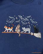 Close-up of colorful witch cats riding a broomstick embroidery with stars and bats on a navy blue sweatshirt