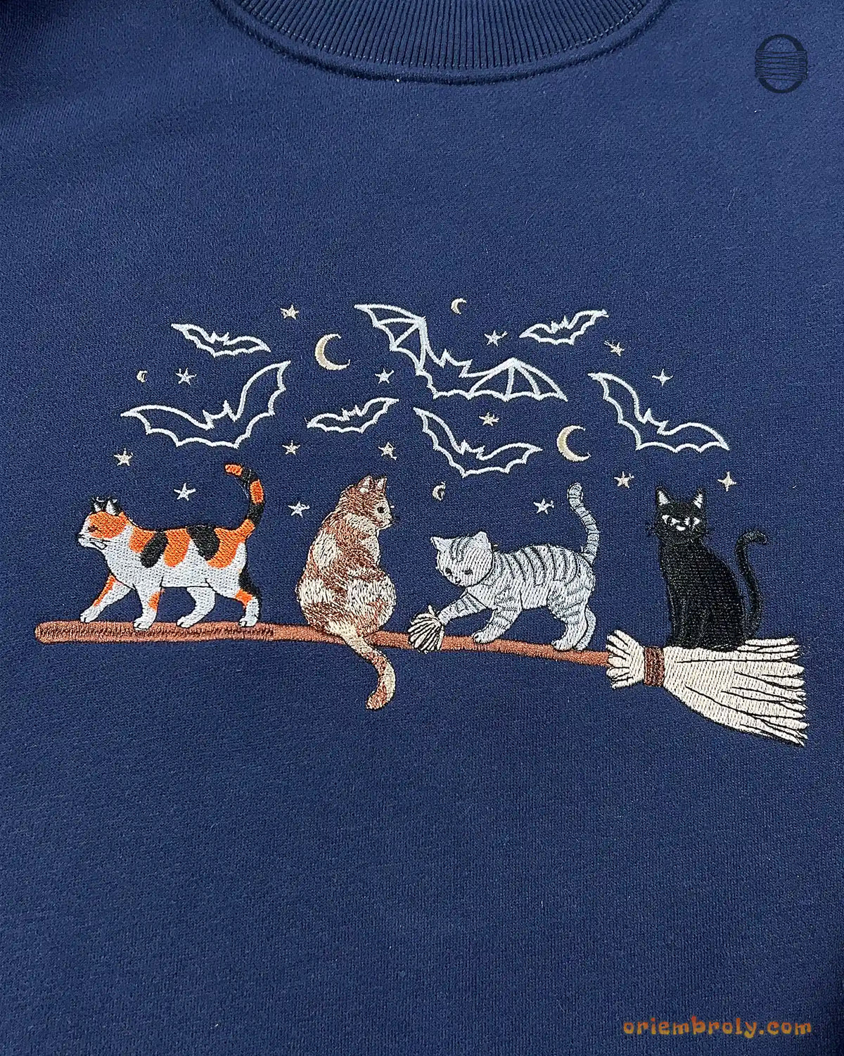 Close-up of colorful witch cats riding a broomstick embroidery with stars and bats on a navy blue sweatshirt