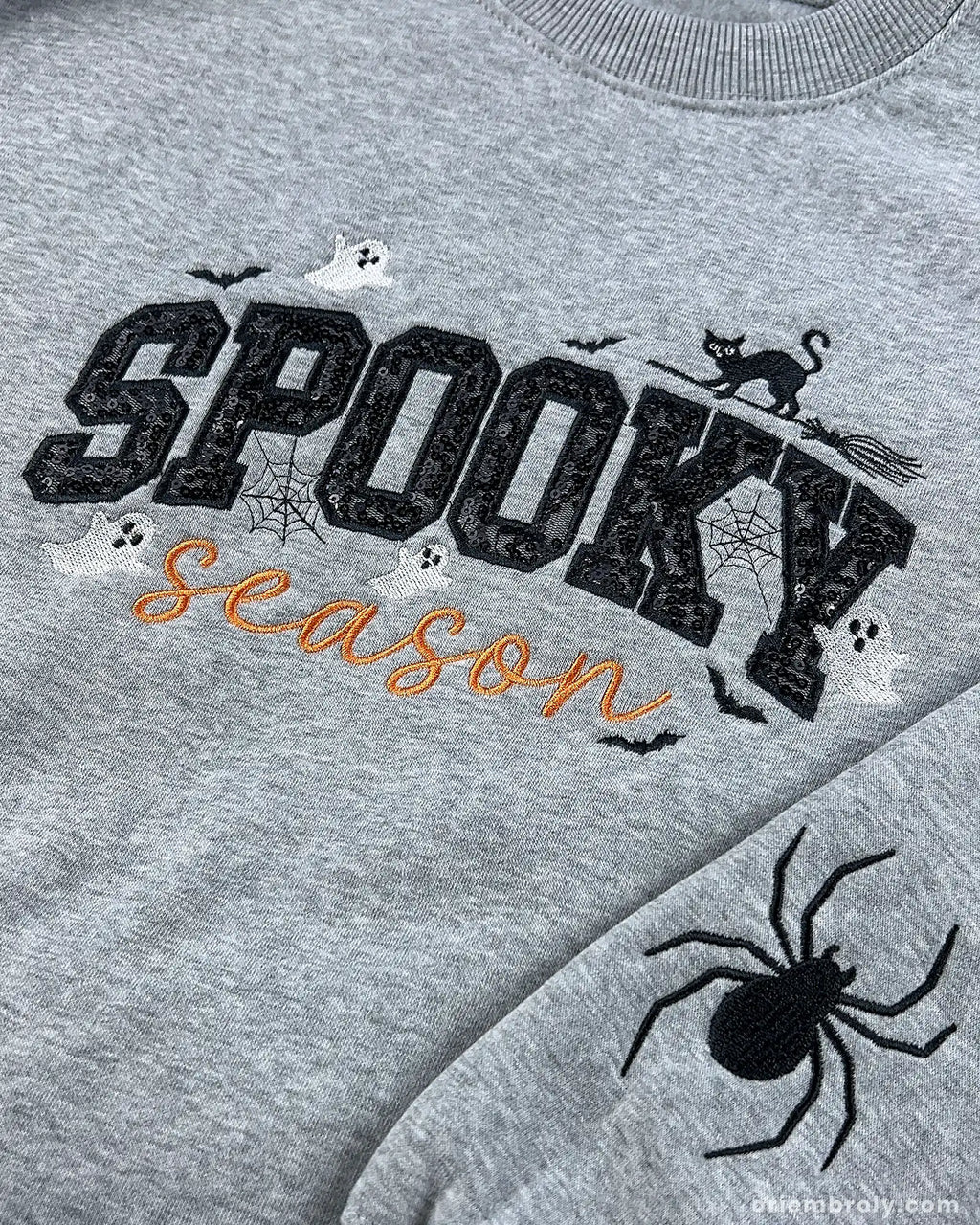 Detailed close-up of spooky season sequin embroidery, cat on broomstick, and sleeve spider on grey sweatshirt.