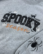 Detailed close-up of spooky season sequin embroidery, cat on broomstick, and sleeve spider on grey sweatshirt.