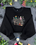Flat lay of a black Hocus Pocus embroidered sweatshirt featuring the Sanderson Sisters, witches broom, and spiderwebs