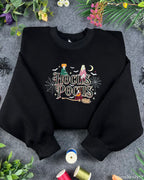 Flat lay of a black Hocus Pocus embroidered sweatshirt featuring the Sanderson Sisters, witches broom, and spiderwebs