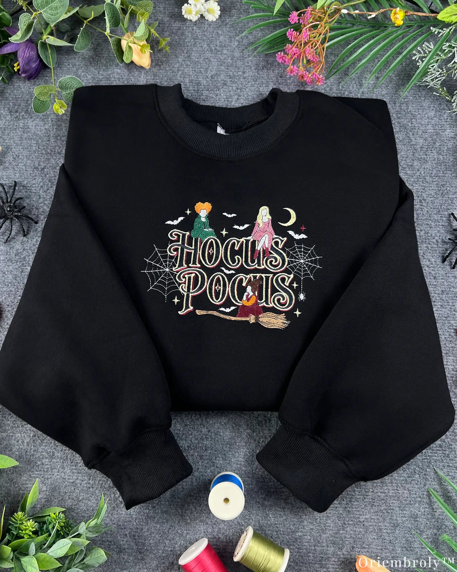 Flat lay of a black Hocus Pocus embroidered sweatshirt featuring the Sanderson Sisters, witches broom, and spiderwebs