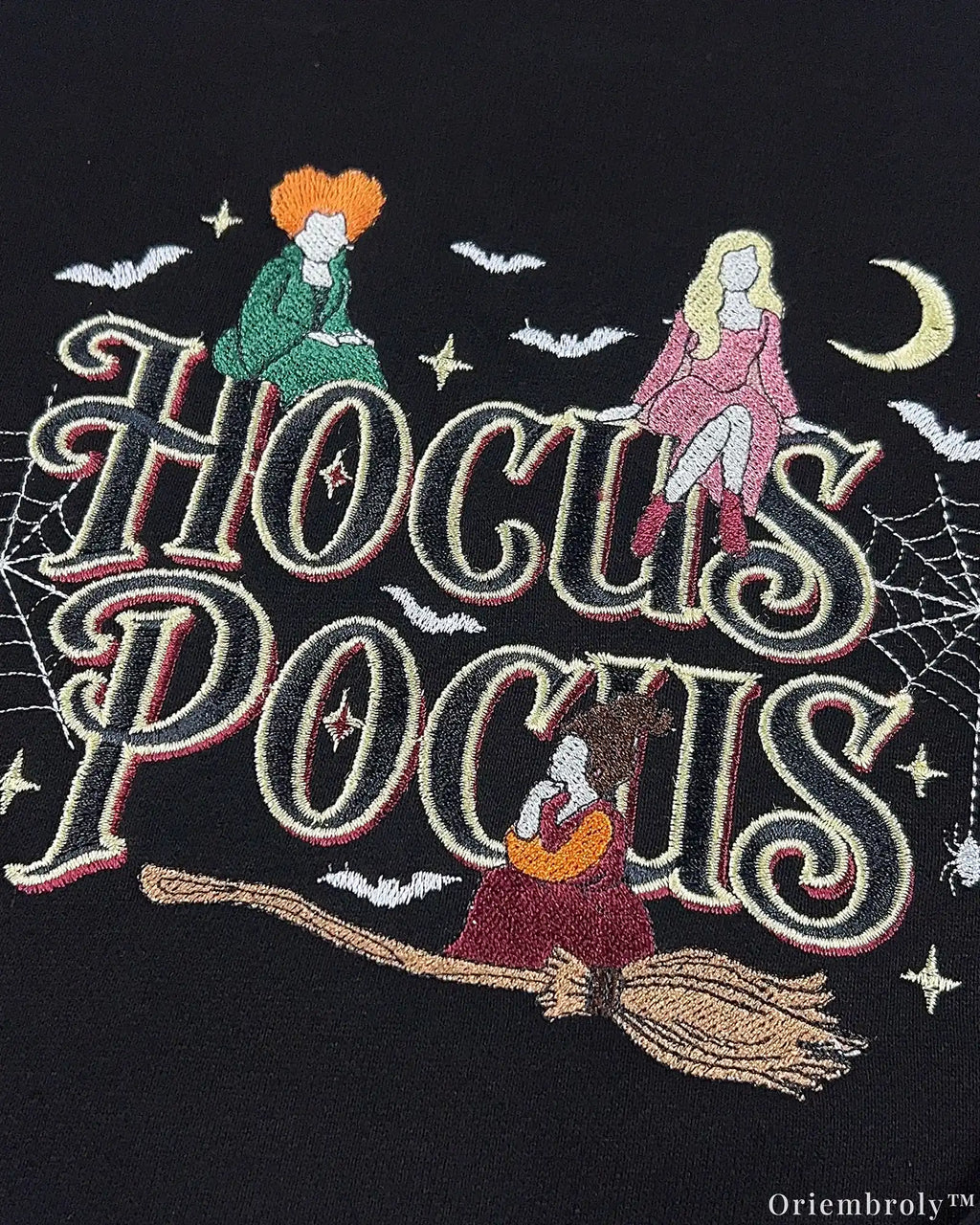 Close-up of Hocus Pocus embroidery design with witches flying on a broomstick, bats, and crescent moon on a black sweatshirt