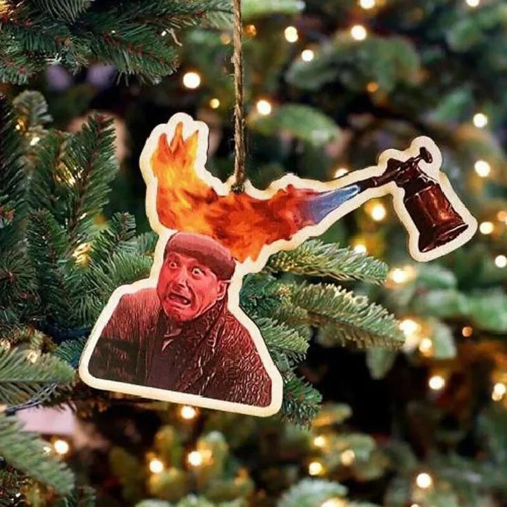 A novelty Christmas tree ornament featuring a cutout image of the character Harry from the movie Home Alone with a blowtorch flame superimposed above his head, referencing the iconic "Harry on fire" scene.