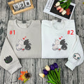 Two folded sweatshirts with dragon designs on a wooden surface with flowers and a calendar.