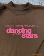 Close-up of hot pink embroidered quote I'd Rather Be Watching Dancing with the Stars on a chocolate brown sweater