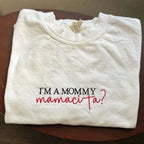 Folded white sweatshirt with text 'I'm a mommy mamacita?' on a wooden surface