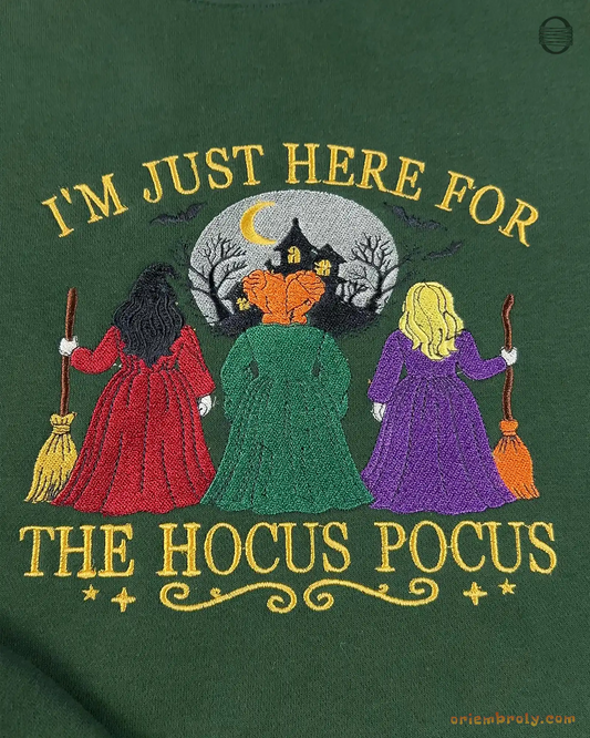 Close-up of Im Just Here For The Hocus Pocus embroidered graphic featuring three witches with brooms on a green sweater