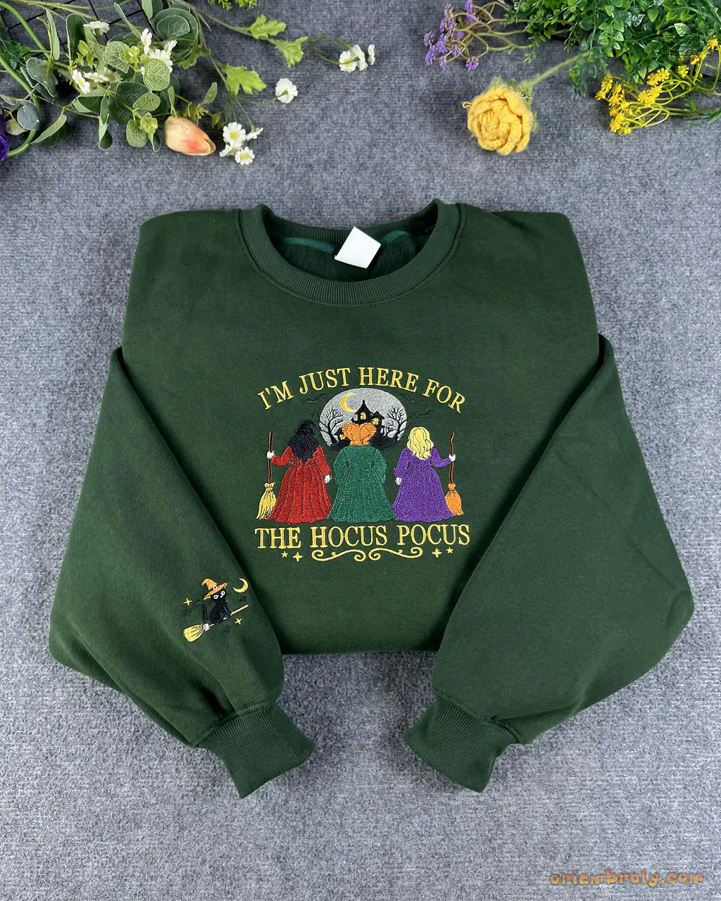 Flat lay of a forest green Halloween crewneck sweatshirt embroidered with Im Just Here For The Hocus Pocus and witches