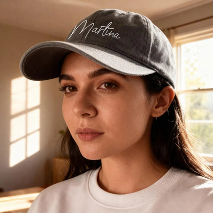 Woman wearing a cap with 'Martina' embroidered on it, sitting indoors by a window.