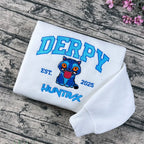 White sweatshirt with 'DERPY' and cartoon character on a wooden surface with flowers.