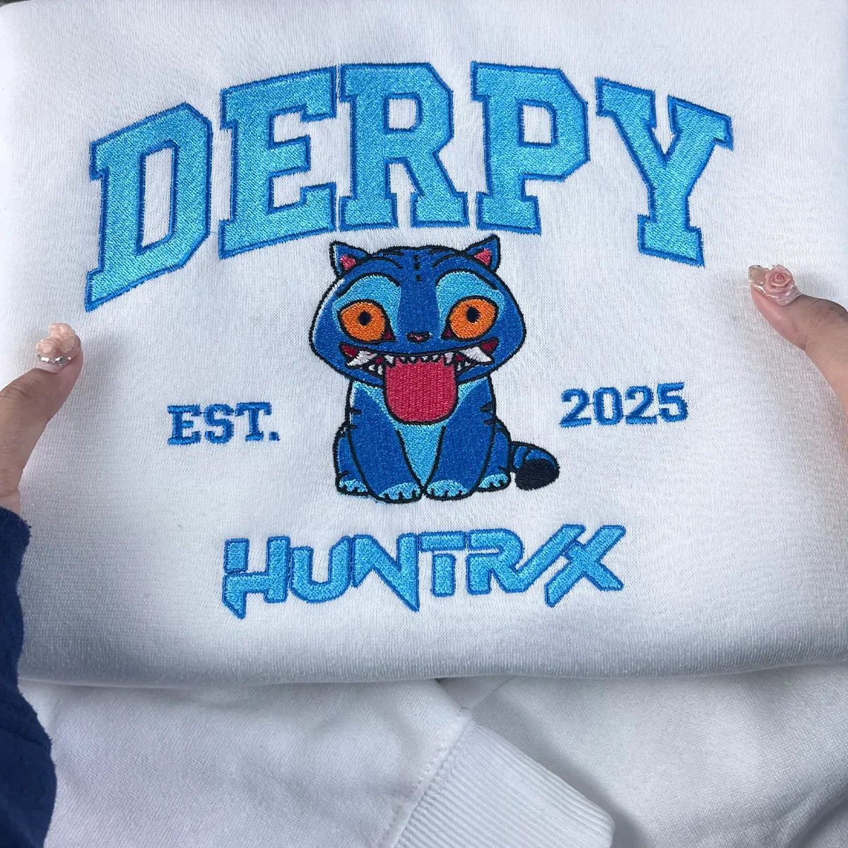 White sweatshirt with blue embroidered text and a cartoon character on a white background