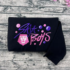 Black sweatshirt with 'SAJA Boys' text and logo on a wooden surface