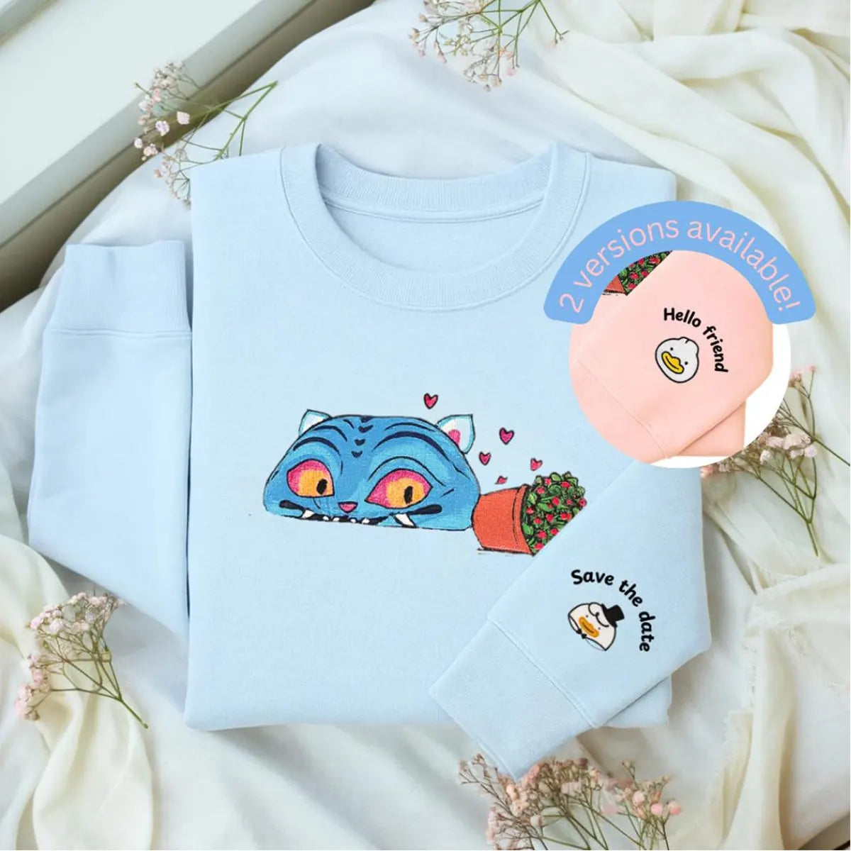 Light blue sweatshirt with a colorful cat design on a white fabric background