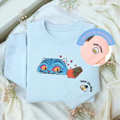 Light blue sweatshirt with a colorful cat design on a white fabric background