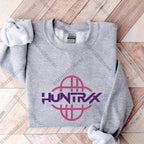 Gray sweatshirt with pink and purple 'HUNTRX' logo on a wooden floor