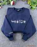 Flat lay of a navy blue crewneck sweatshirt embroidered with gothic bookish symbols and Lady Death sleeve embroidery