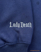 Close-up of Lady Death embroidered in gothic font on the sleeve of a navy blue sweatshirt