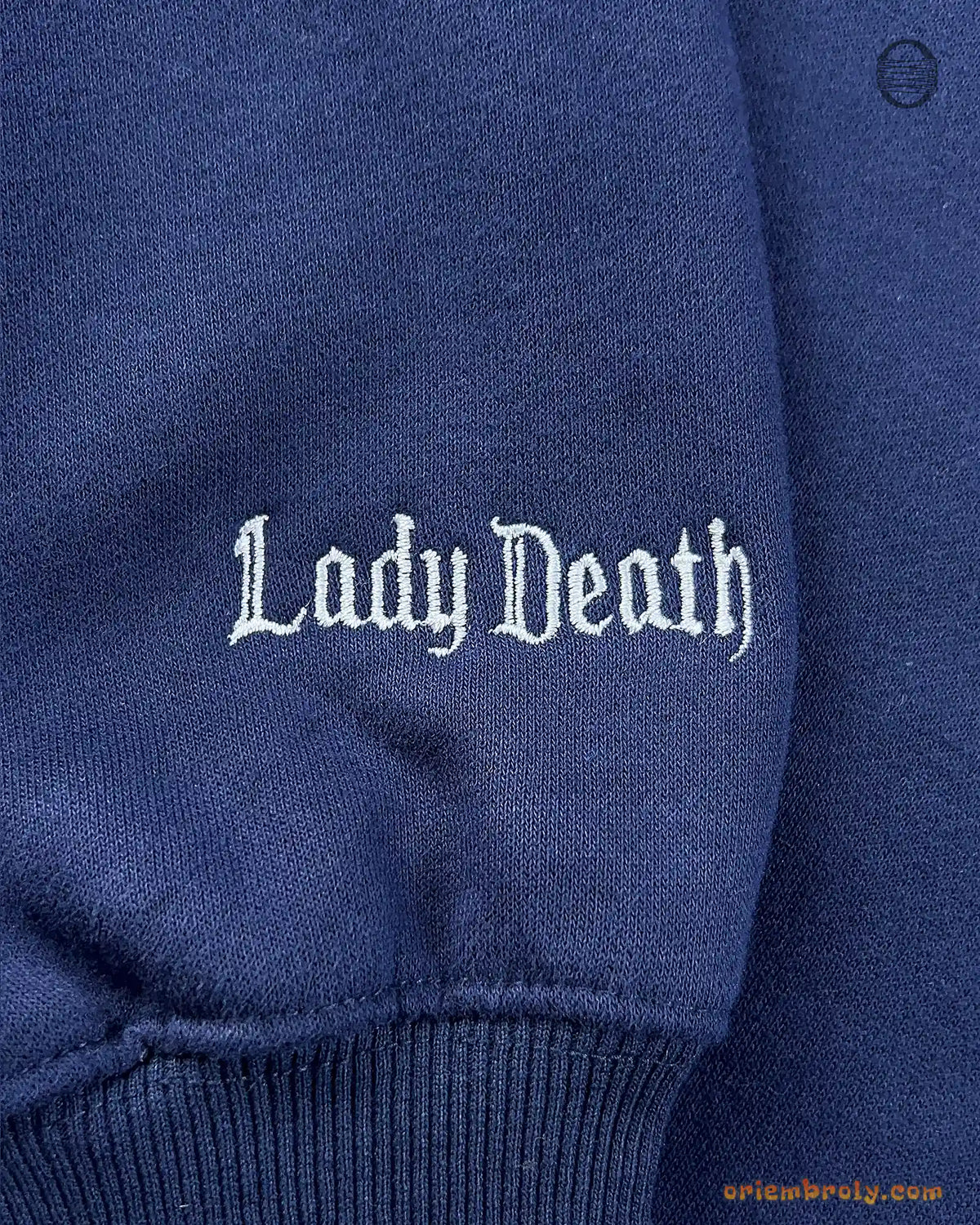 Close-up of Lady Death embroidered in gothic font on the sleeve of a navy blue sweatshirt