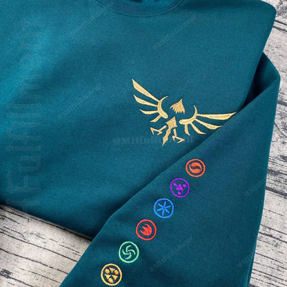 Teal hoodie with gold emblem and colorful symbols on a wooden surface