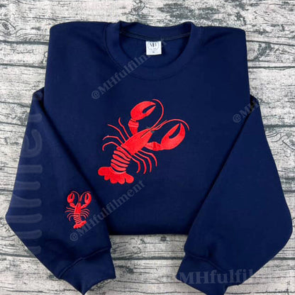 Navy blue sweatshirt with red lobster design on a gray wooden surface