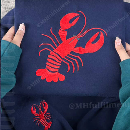 Navy blue sweatshirt with red lobster design held by a person wearing teal sleeves.