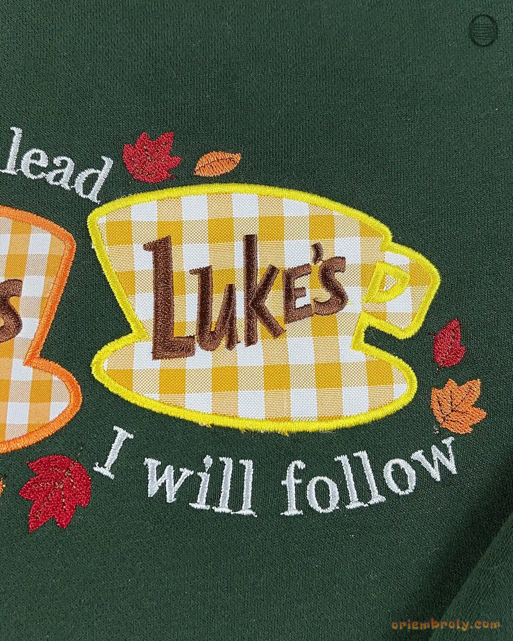 Detailed view of Lukes Diner coffee cup embroidery with I Will Follow text on a forest green crewneck sweatshirt