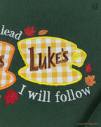 Detailed view of Lukes Diner coffee cup embroidery with I Will Follow text on a forest green crewneck sweatshirt