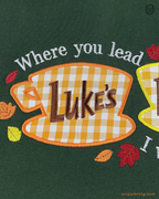 Close-up of Lukes Diner yellow coffee cup embroidery with Where You Lead quote and autumn leaves on a green sweater