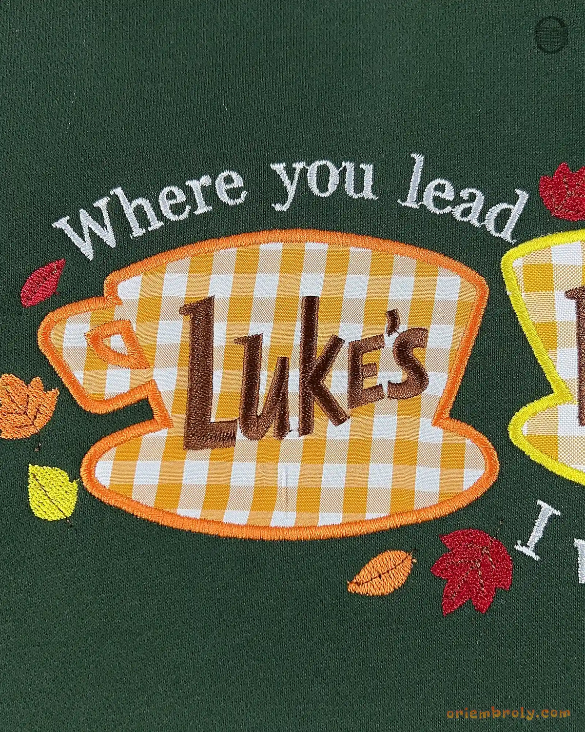 Close-up of Lukes Diner yellow coffee cup embroidery with Where You Lead quote and autumn leaves on a green sweater