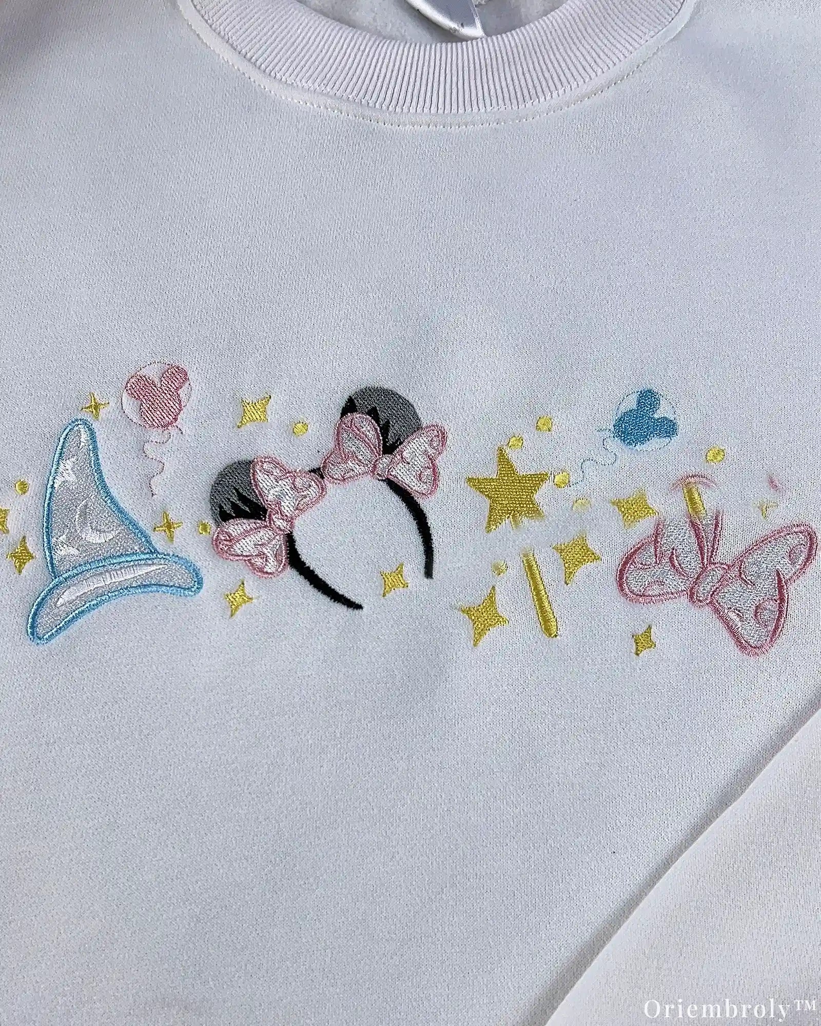 Close-up of pastel Disney embroidery design with Minnie ears, magic wand, sparkles, and bow on a white crewneck sweater
