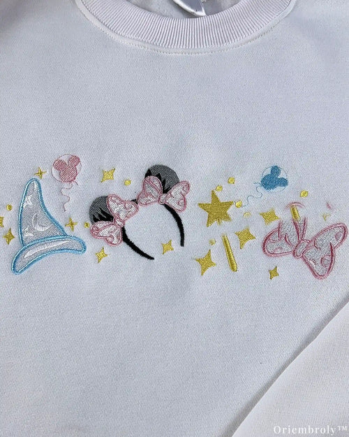Close-up of pastel Disney embroidery design with Minnie ears, magic wand, sparkles, and bow on a white crewneck sweater