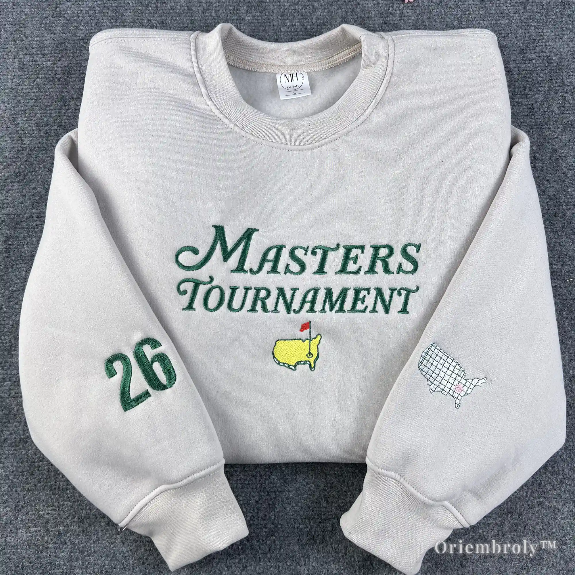 Premium cream crewneck sweatshirt featuring green Masters Tournament embroidery and the iconic Augusta National logo. High-quality golf apparel with custom "26" sleeve patch for 2026 tournament fans