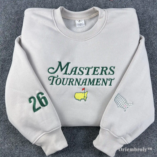 Premium cream crewneck sweatshirt featuring green Masters Tournament embroidery and the iconic Augusta National logo. High-quality golf apparel with custom "26" sleeve patch for 2026 tournament fans