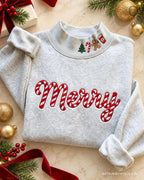 Flat lay of an ash grey crewneck sweatshirt embroidered with red candy cane Merry chest text and cute Christmas collar icons