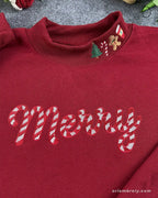 Close-up of white candy cane Merry embroidery and Christmas tree gingerbread stocking embroidered collar on a red sweater