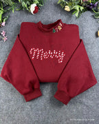 Flat lay of a maroon red crewneck sweatshirt embroidered with candy cane pattern Merry text and Christmas collar details