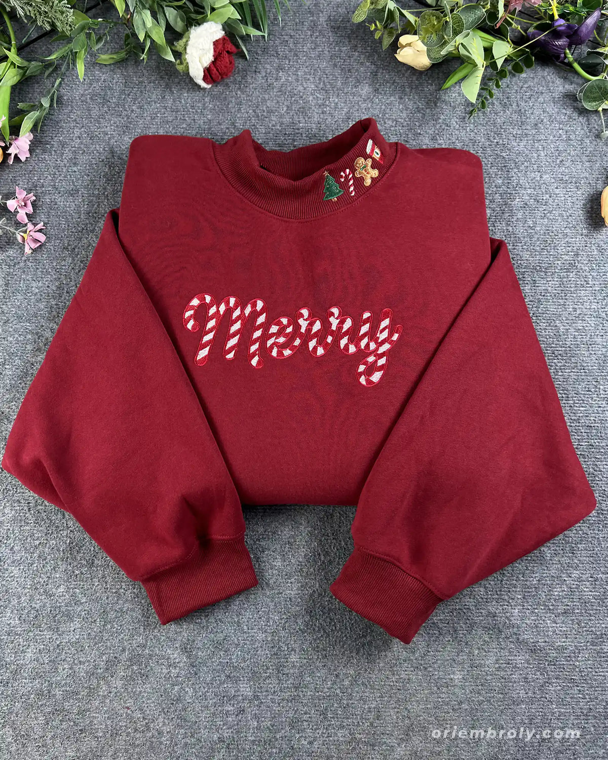 Flat lay of a maroon red crewneck sweatshirt embroidered with candy cane pattern Merry text and Christmas collar details