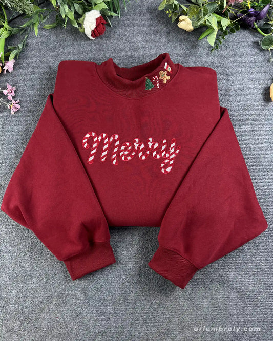 Flat lay of a maroon red crewneck sweatshirt embroidered with candy cane pattern Merry text and Christmas collar details